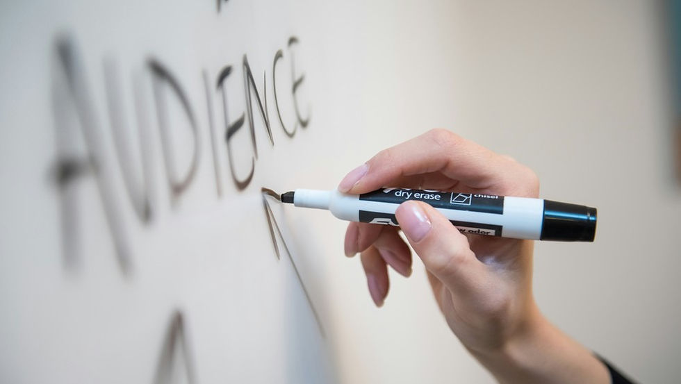 Hand writes on a whiteboard with a dry-erase marker beside the word AUDIENCE in soft focus.