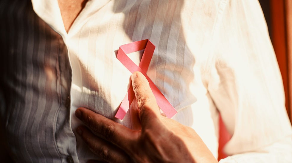 Close-up of a hand pinning a pink awareness ribbon to a white shirt in warm light.