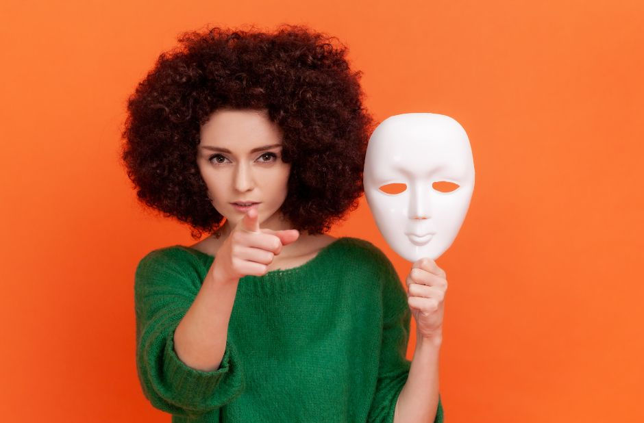 The image shows a woman with curly hair wearing a green sweater, standing against an orange background. 