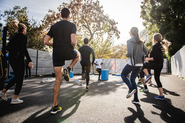 A group of people is exercising outdoors together, performing high-knee drills on a sunny day.
