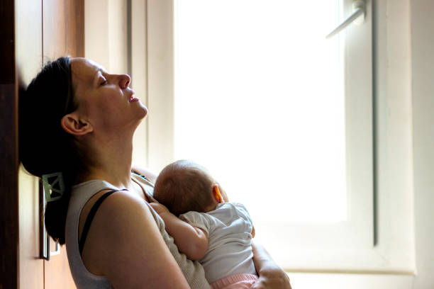 Smiling mother cradles newborn in a hospital bed, black-and-white scene with staff nearby.