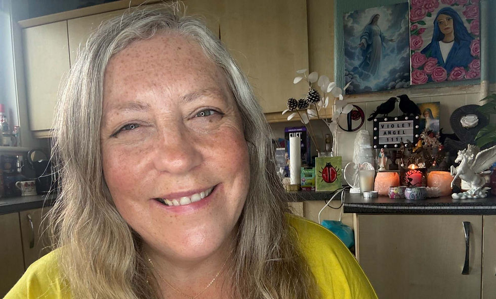Smiling gray-haired woman in a cozy room with candles, art, and a sign reading VIOLET ANGEL 1111.