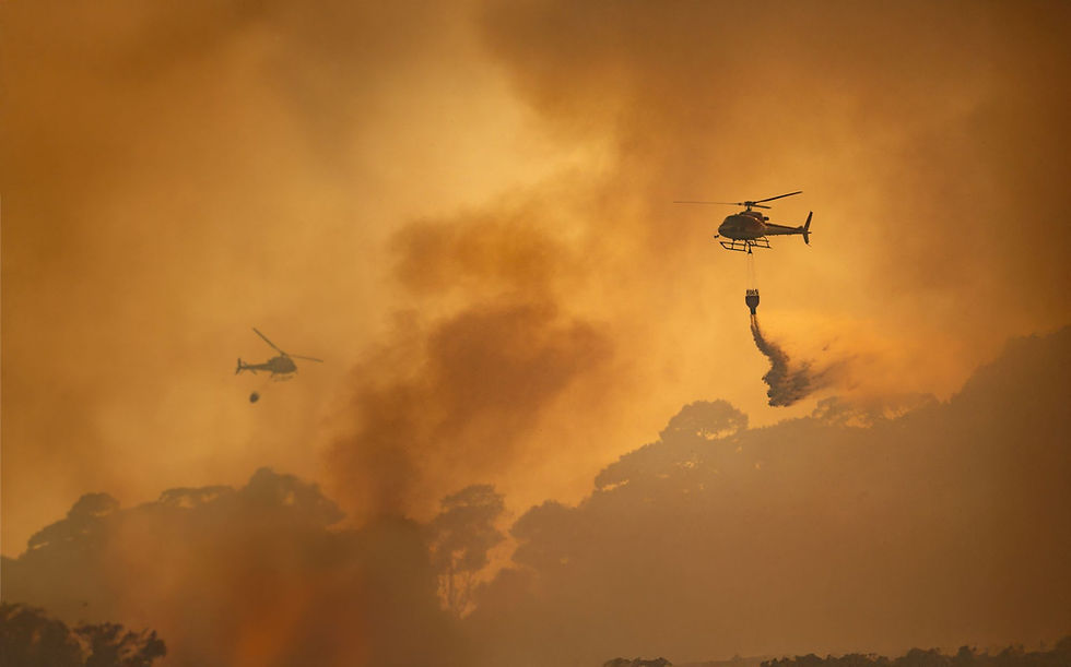 Helicopters drop water over a forest fire, engulfed in orange smoke. Silhouetted trees in the background create a tense atmosphere.
