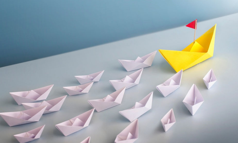 Yellow paper boat with red flag leads several white paper boats on a pale blue surface, symbolizing leadership and direction.