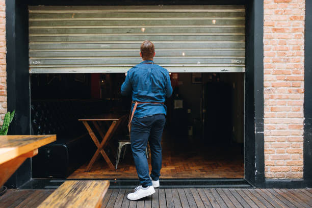 A man is opening a metal shutter to a café or restaurant, preparing to start the day.