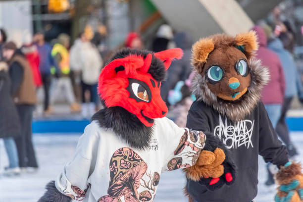 Two people in colorful animal costumes ice skate in a rink, holding hands. Background shows other skaters and blurred winter attire.