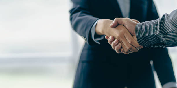 A close up of two people in business attire shaking hands, symbolising agreement, negotiation, or professional interaction.