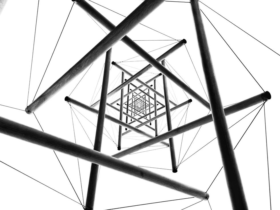 Looking up at a geometric structure of intersecting rods and cables against a white background, creating a striking black and white pattern.