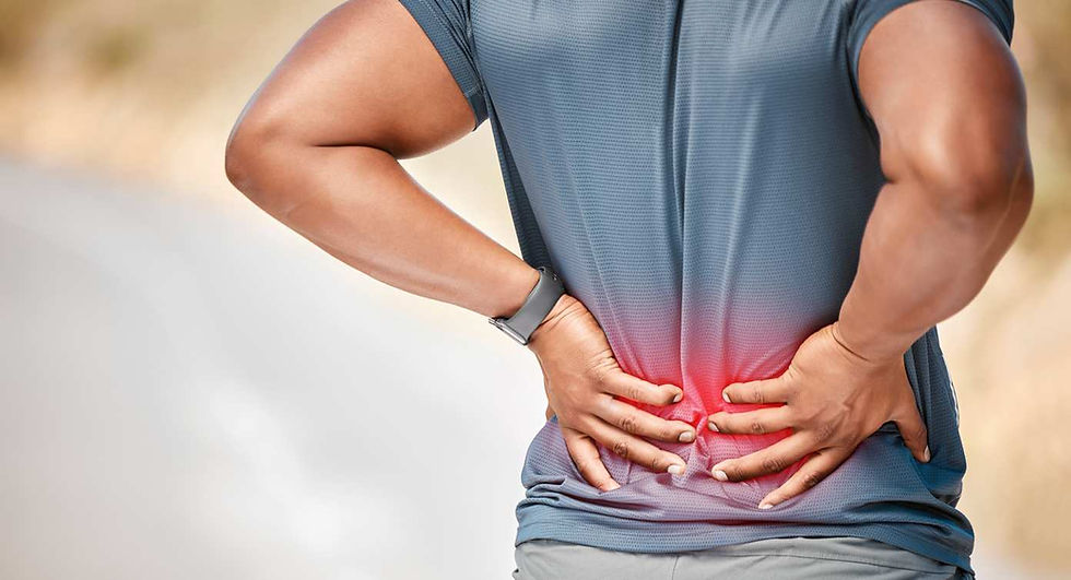 Person in blue shirt holds lower back in pain, with red highlight indicating discomfort. Outdoors, blurred background, wearing a watch.