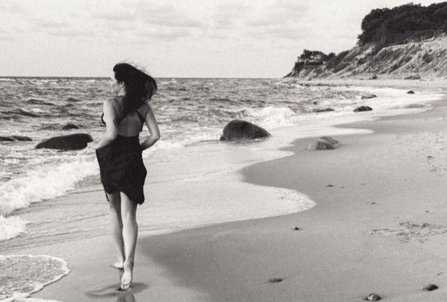 A woman walking along a beach next to the ocean.