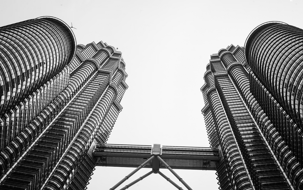 Black and white image of two skyscrapers with a connecting skybridge, viewed from below against a clear sky, showcasing modern architecture.