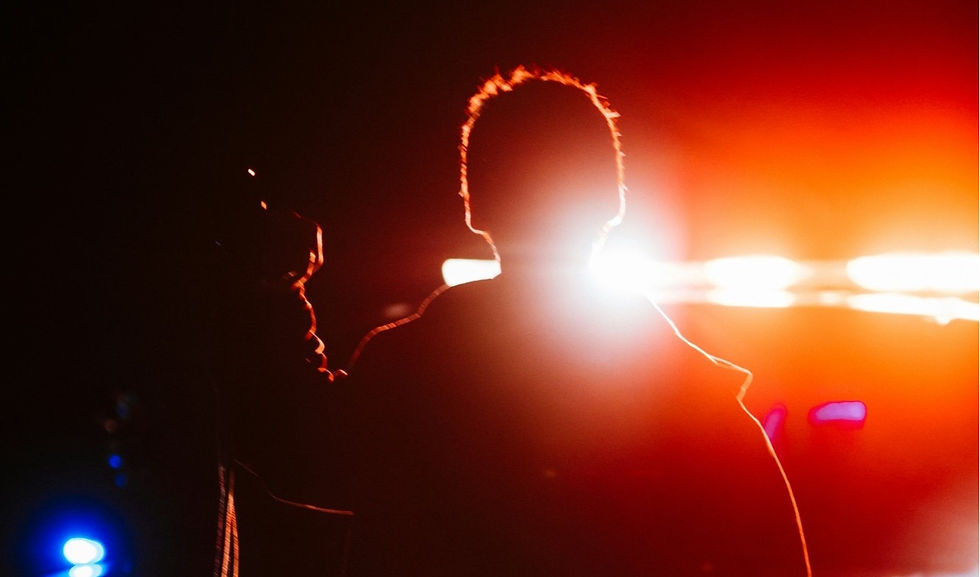 Silhouetted person stands before blinding red-orange stage lights, with a partial profile at left, creating a dramatic mood.