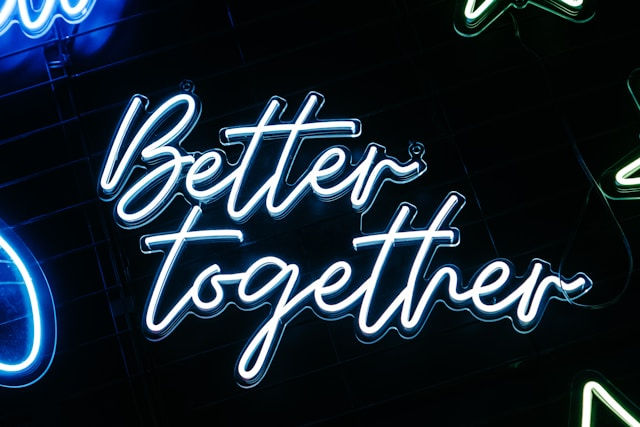 Blue neon script sign reading Better together on a dark background, glowing with a lively, upbeat feel.