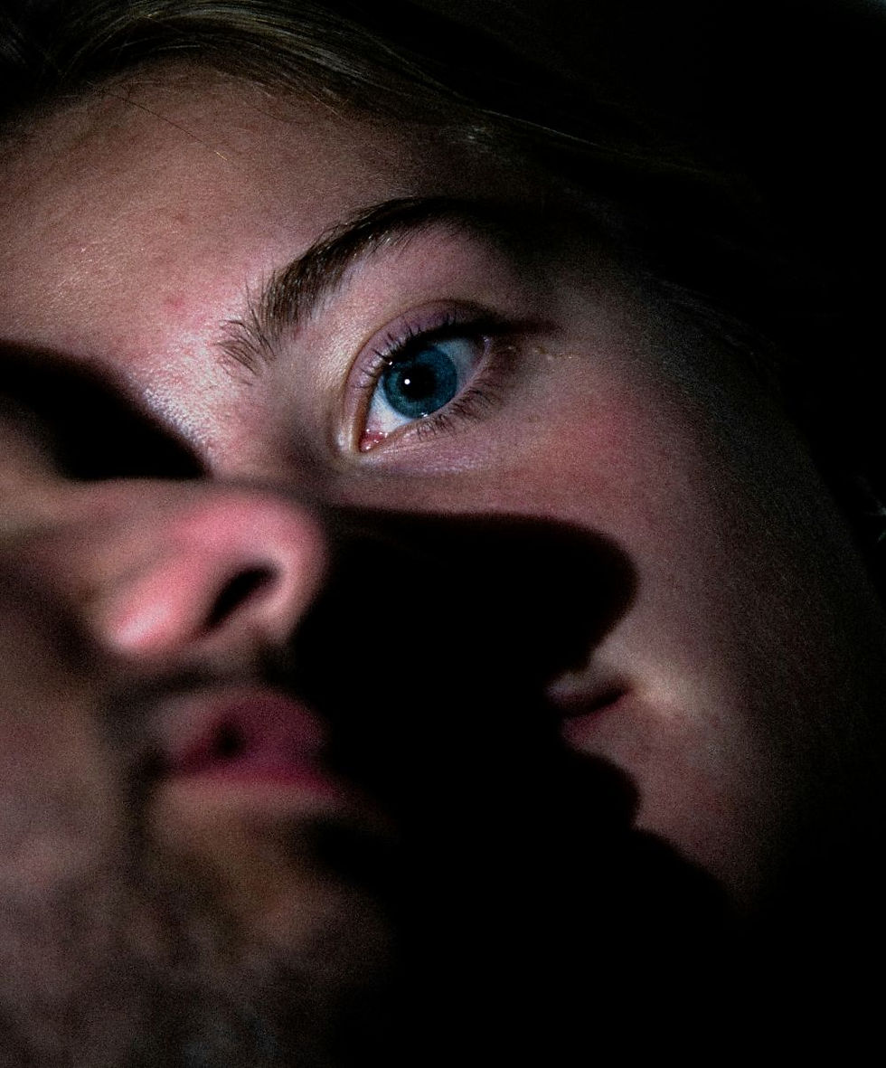 Close-up of a person's blue eye with another person's face partially visible in shadow. The mood is intense and dramatic.