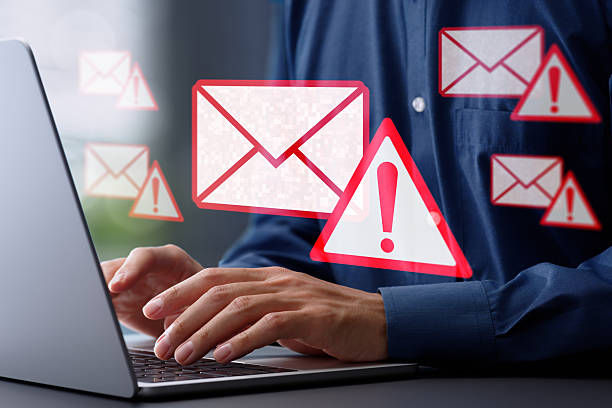Hands typing on a laptop with red email and exclamation icons floating, indicating email alerts or spam warnings, set in an office.