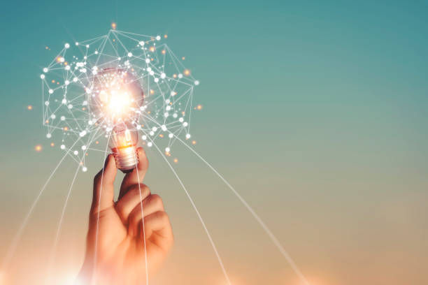 Hand holding a glowing light bulb with a network of connections around it, set against a gradient sky background, symbolizing innovation.
