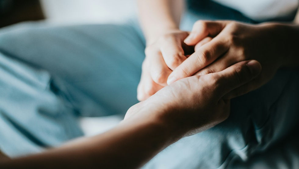 Close-up of two people holding hands on a lap, suggesting comfort and support in a soft blue setting