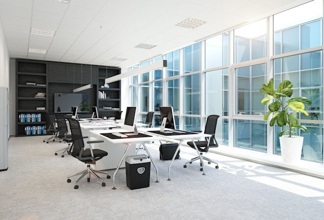 The photo shows a modern, well-lit office space with large windows allowing ample natural light. 