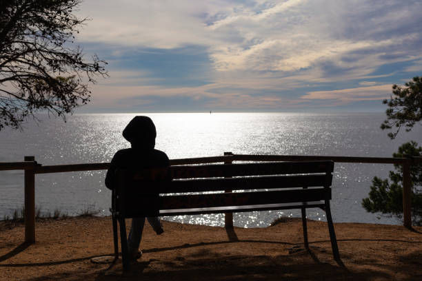 shot of an unrecognizable person sitting on a bench overlooking the sea