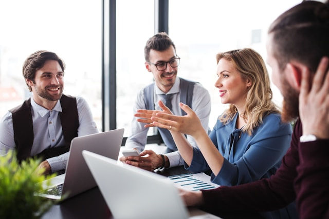 A group of four business professionals are having a meeting around a table with laptops and documents.