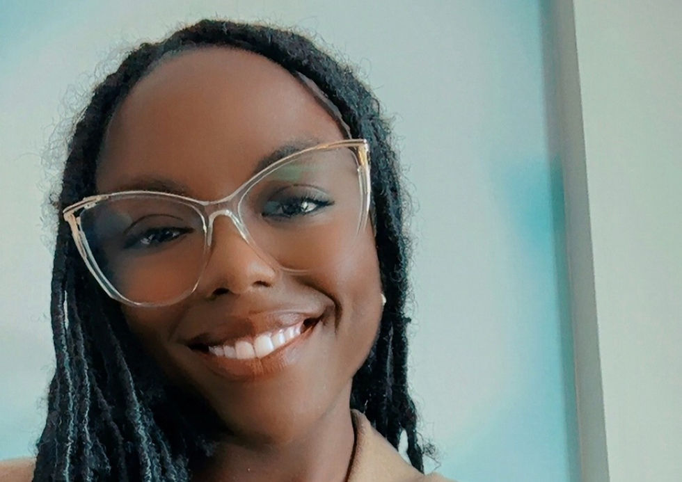 Smiling person with glasses and long hair poses against a soft, light background, conveying joy and warmth.