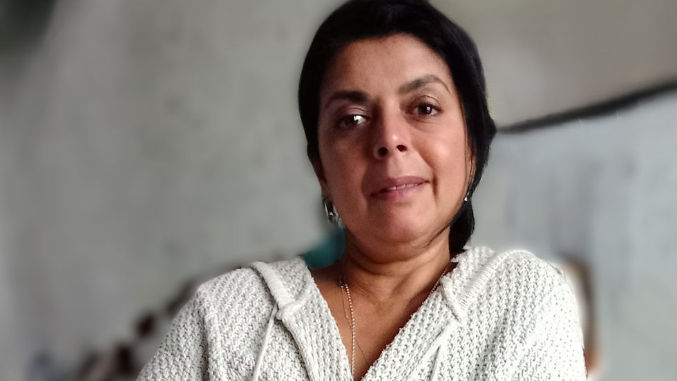 Woman in a white knit sweater smiles softly, sitting indoors with a blurred gray background, creating a calm and cozy atmosphere.