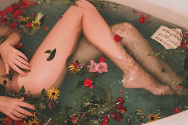 Person relaxing in a bathtub filled with water, surrounded by colorful flowers and a music sheet. Calm and serene mood.