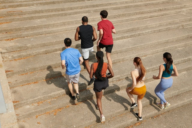 Six people in athletic wear run up outdoor concrete steps. Bright clothing includes blue, red, and orange. The mood is energetic and active.