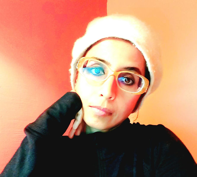 A person wearing glasses and a white hat leans on their hand. The background is red and orange, creating a warm and contemplative mood.