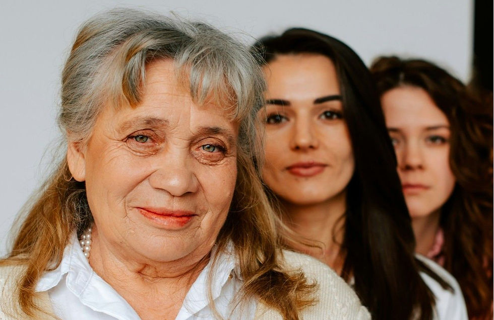 Portrait of three women indoors, older woman in front with two younger women behind, all facing camera with calm expressions