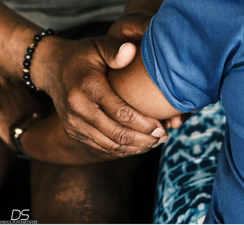 A close-up of a hand gently holding an arm in a blue shirt, evoking a sense of care. The background shows a patterned fabric.
