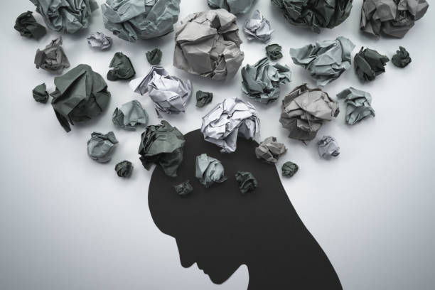 Silhouette of a person with crumpled paper balls above them on a gray background, symbolizing stress or overthinking.