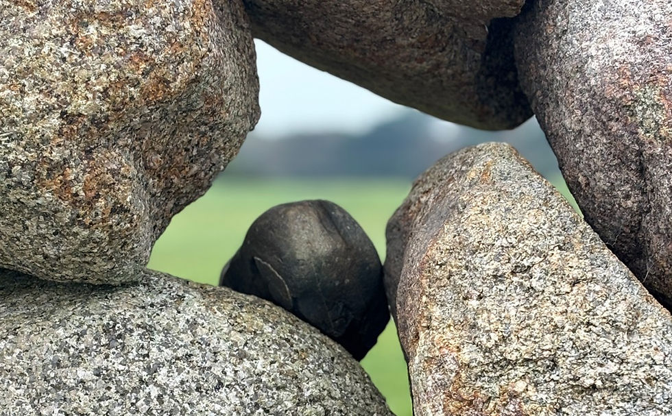 Granite stones frame a small black stone, with a blurred green field and sky in the background.