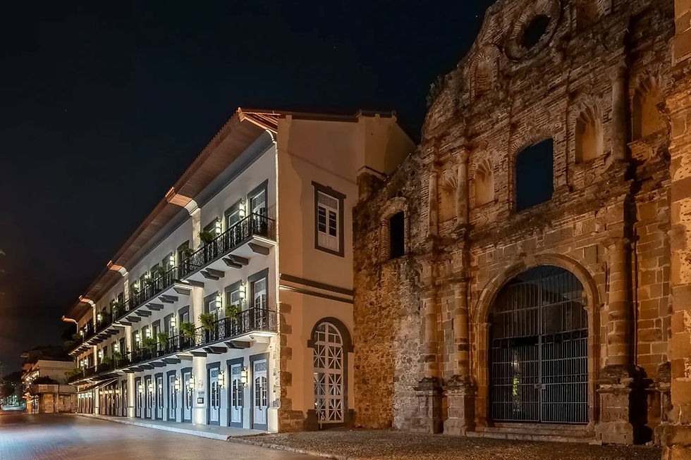 Night street with a lit colonial building beside an old stone church facade under a dark sky.