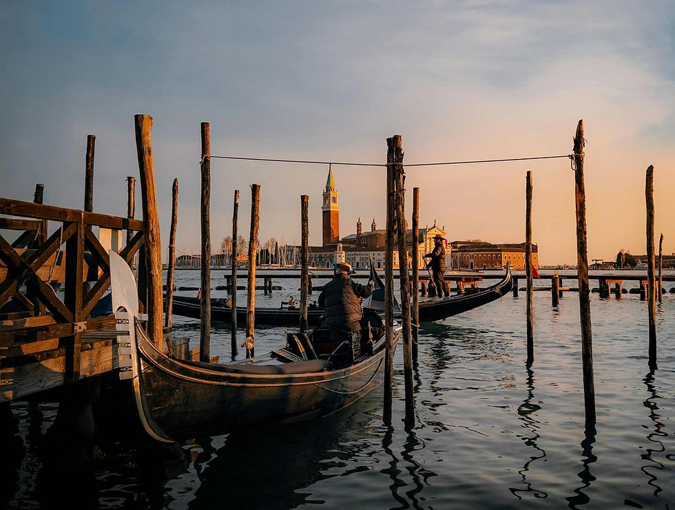 Gondolas float on Venice's canals at sunset. Gondoliers navigate under a sky tinged with warm hues, silhouetted poles and historic buildings.