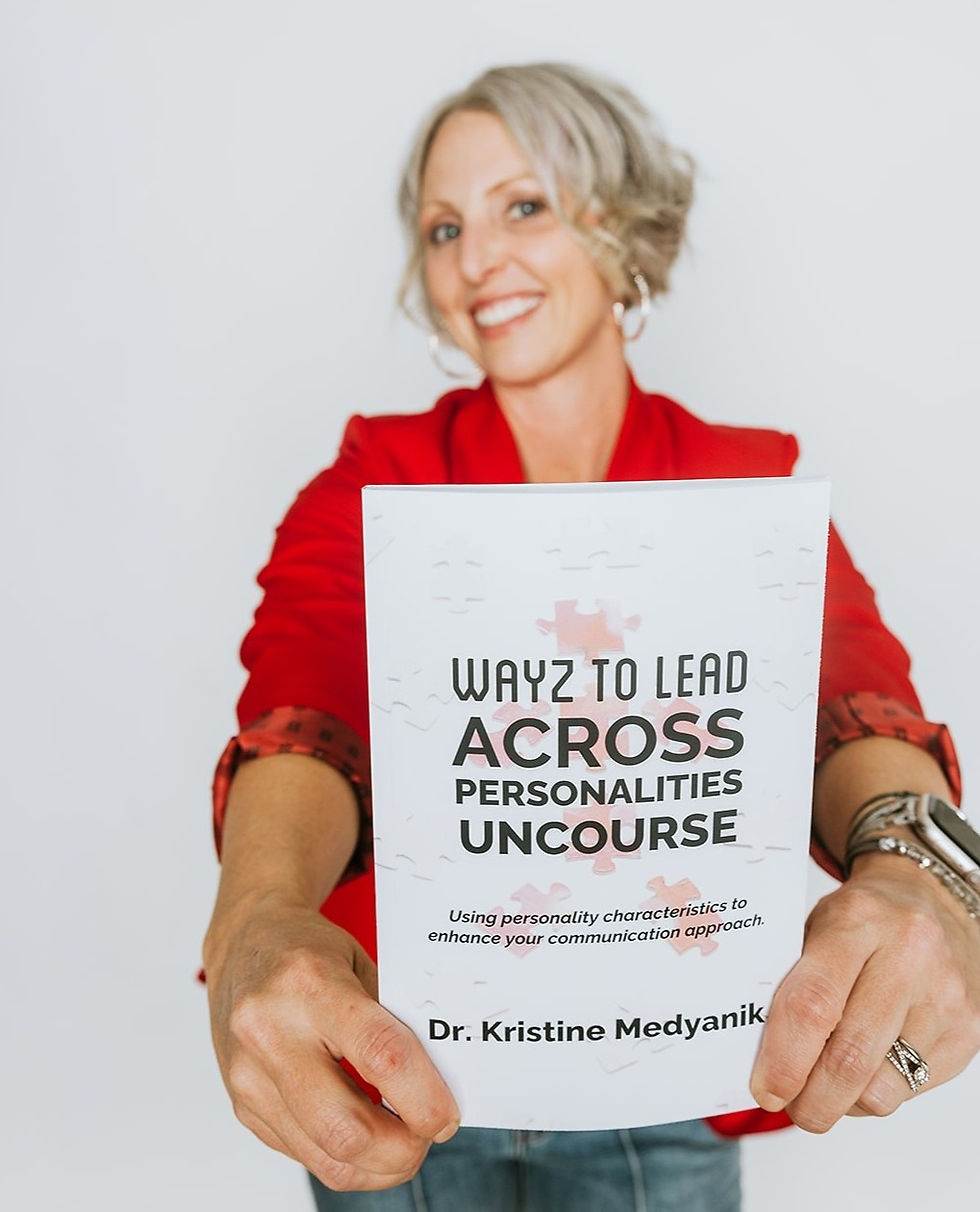 Smiling person in a red jacket holding a book titled "Wayz to Lead Across Personalities Uncourse" by Dr. Kristine Medyanik, against a white background.