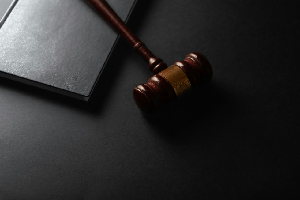 Wooden judge’s gavel beside a black book on a dark surface, dramatic legal-themed still life with no visible text.