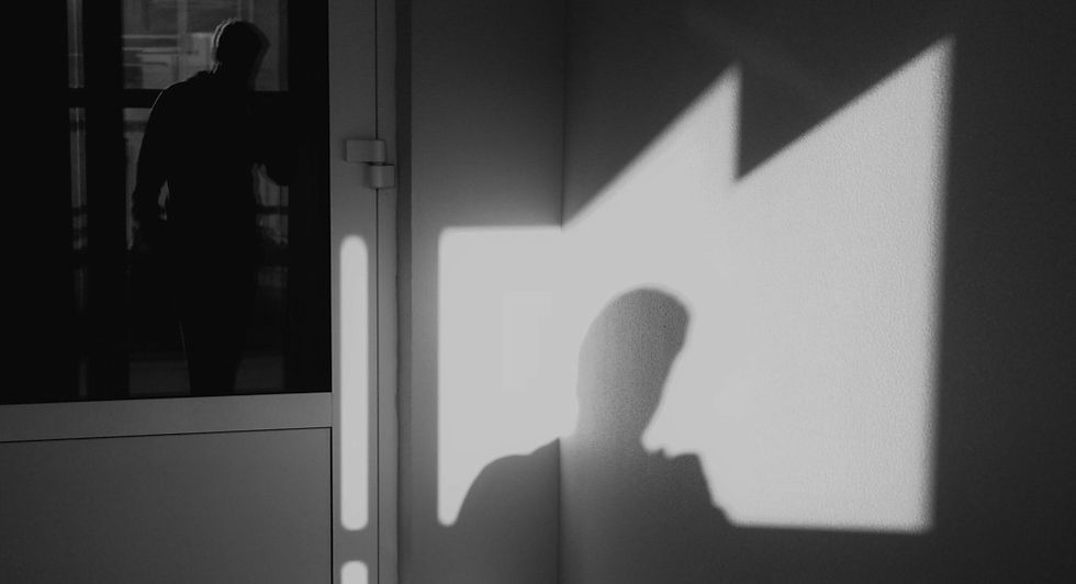 Black-and-white silhouette of a person on a wall beside a glass door, with another figure reflected in the pane.