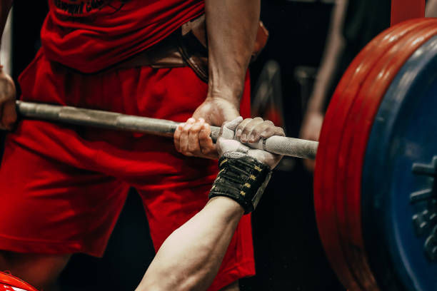 Weightlifter in red shorts lifting a barbell with heavy blue and red plates. Focused, intense effort in a gym setting.