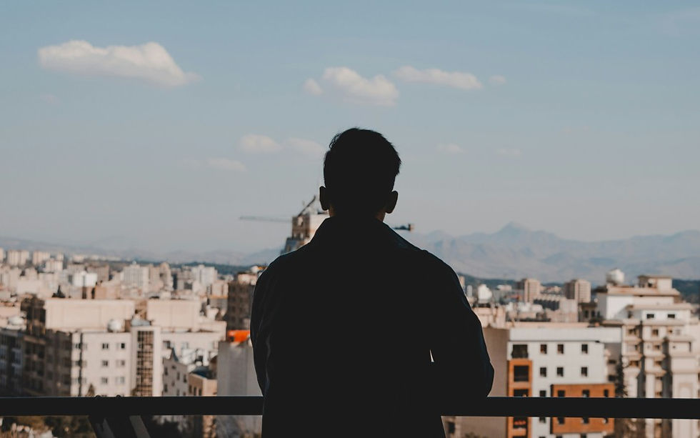 Silhouette of a man on a balcony overlooking a city skyline and distant mountains under a blue sky with clouds.