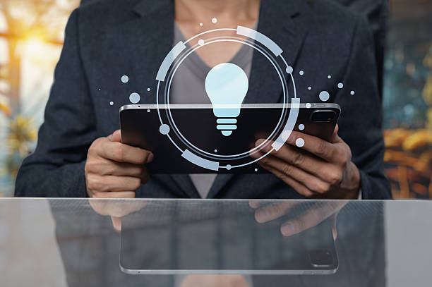 Person in a suit holding a tablet, overlaid with a glowing light bulb icon, conveying innovation. Blurred colorful background.