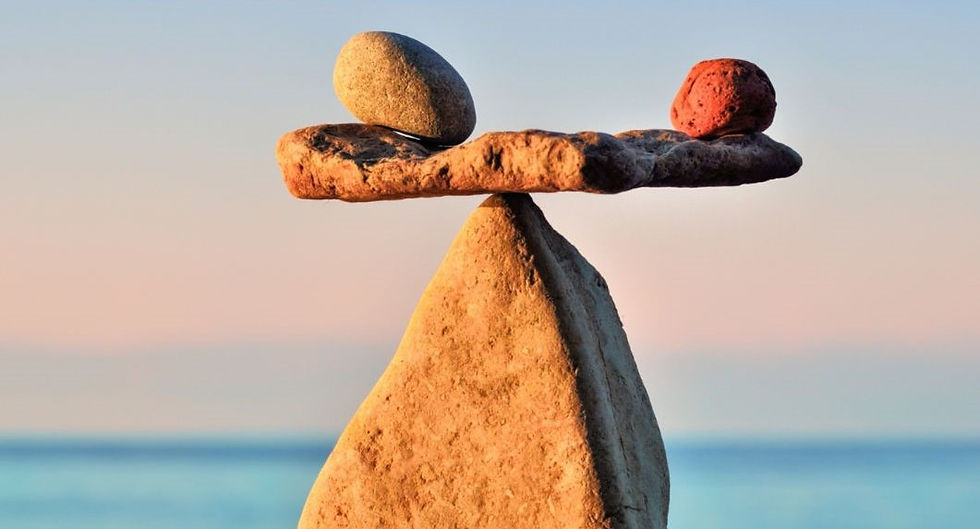 Stacked stones balancing by the sea at sunset. One grey and one red stone on a flat rock, creating a serene, harmonious scene.