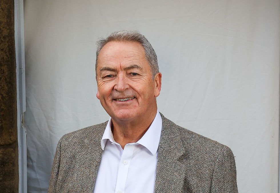 Smiling man in a grey tweed jacket and white shirt stands against a plain white background, exuding a friendly, approachable mood.