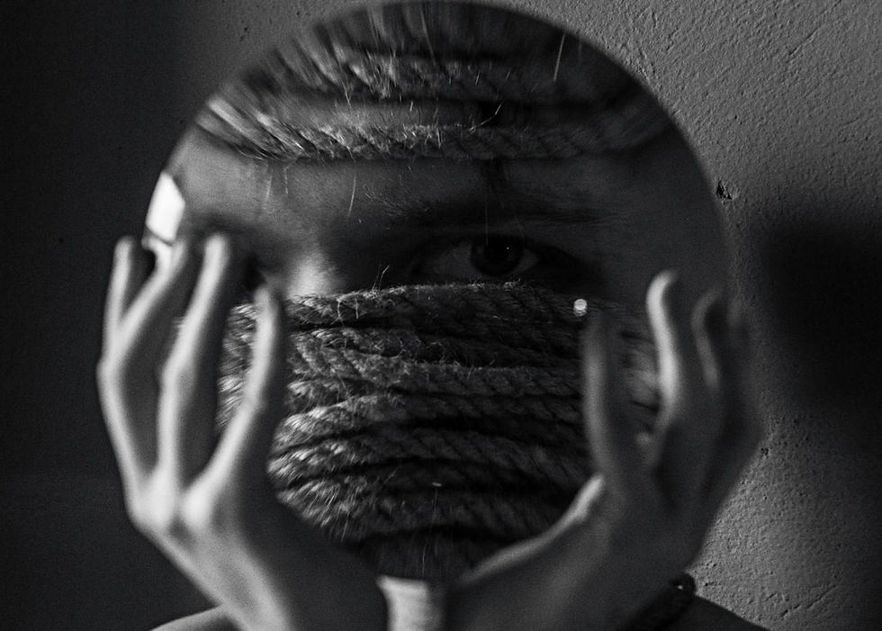 B&W image of a person's face seen through a round mirror. They hold the mirror, eyes visible behind ropes wrapped across their face. Mysterious vibe.