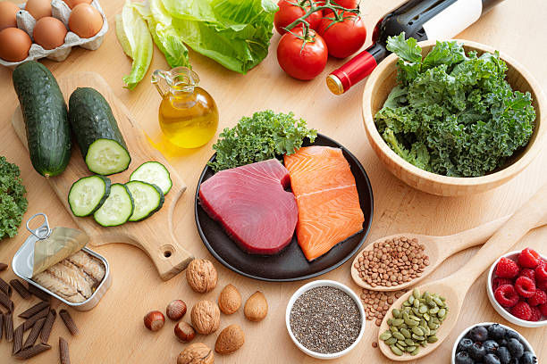 Healthy foods on a wooden table: fish, kale, cucumbers, tomatoes, berries, nuts, seeds, eggs and olive oil.