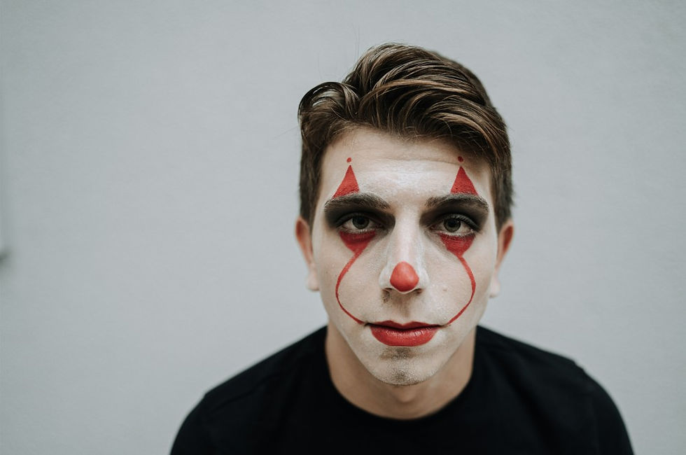 Portrait of a serious person with clown face paint and red nose against a plain gray background