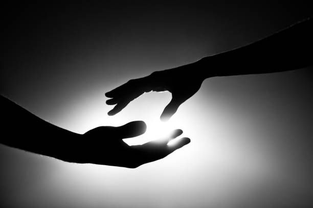 Silhouettes of two hands reaching for each other against a bright background, conveying a mood of connection and support.