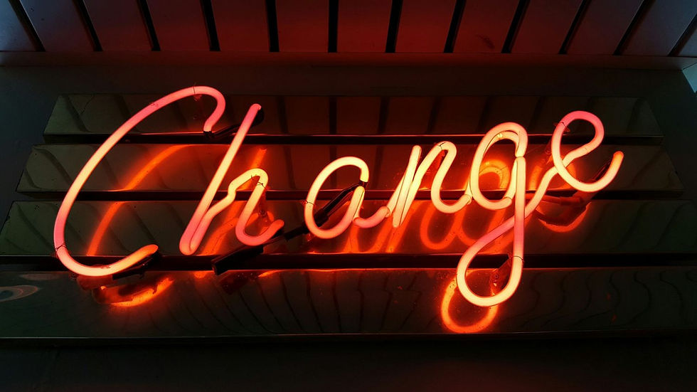 Neon sign spelling "Change" in bright red-orange against a dark, reflective background, creating a vibrant, dynamic mood.