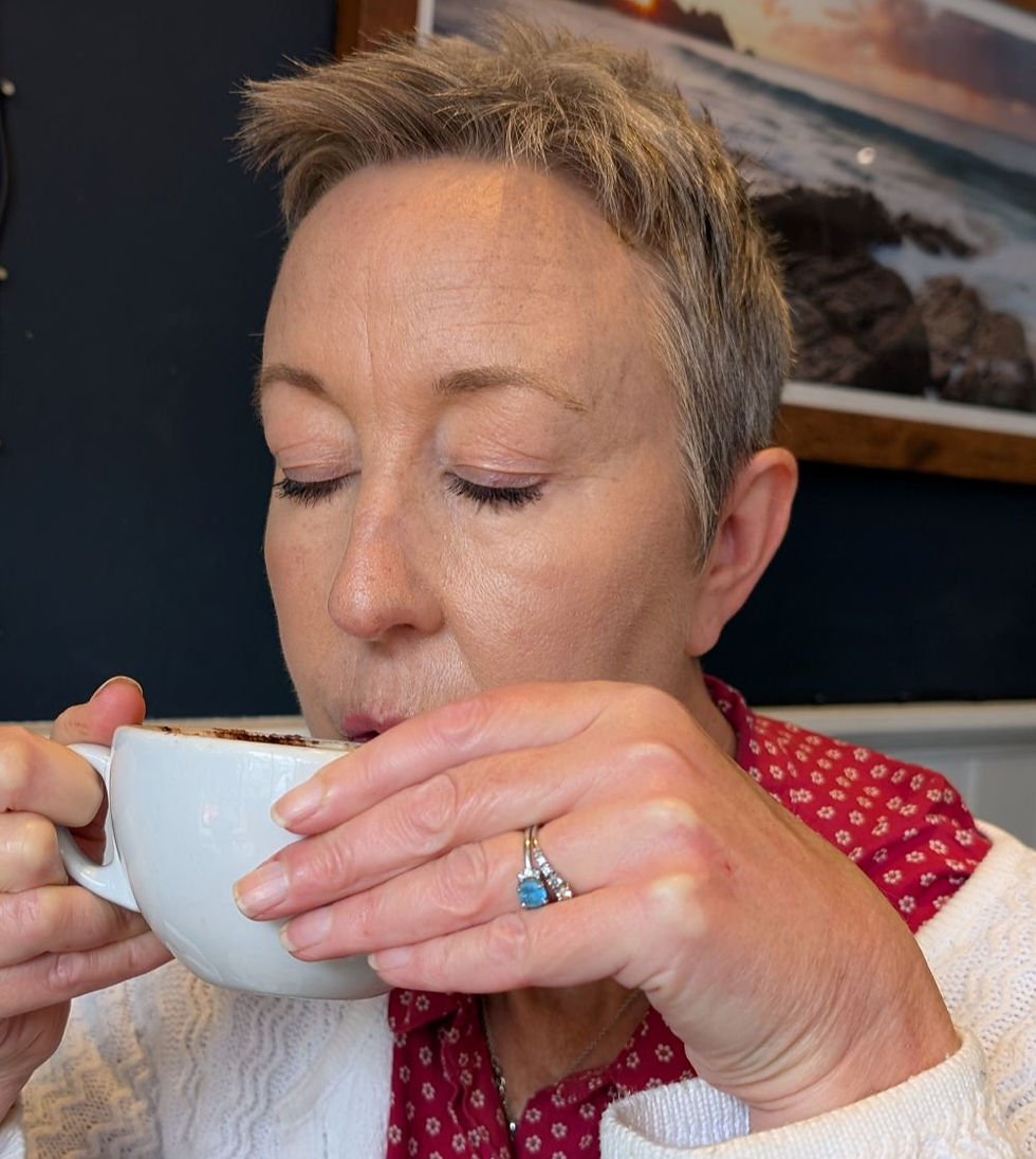 Close-up of a woman sipping from a white coffee cup indoors, eyes closed, wearing a red patterned scarf and white sweater.