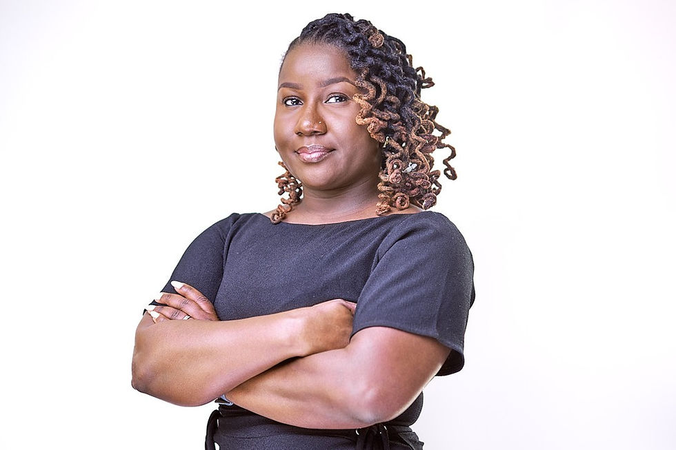 Person in a black shirt with cross-armed stance, smiling confidently against a plain white background. Curly hair highlighted with brown.